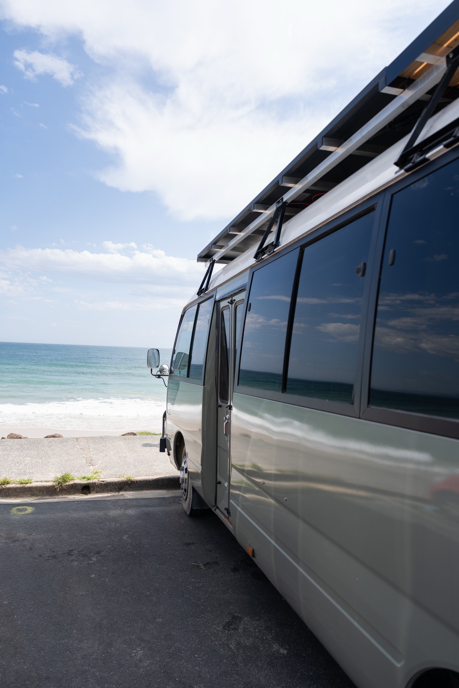 Sage Toyota Coaster pop-top beside the ocean